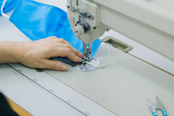 Stepwise stitching of blue fabric medical masks on a sewing machine. A close up of an industrial sewing machine makes a seam. - Foto, afbeelding