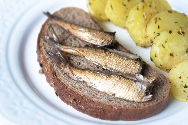 Canned sprats on rye bread served with herb baked potatoes - Photo, Image
