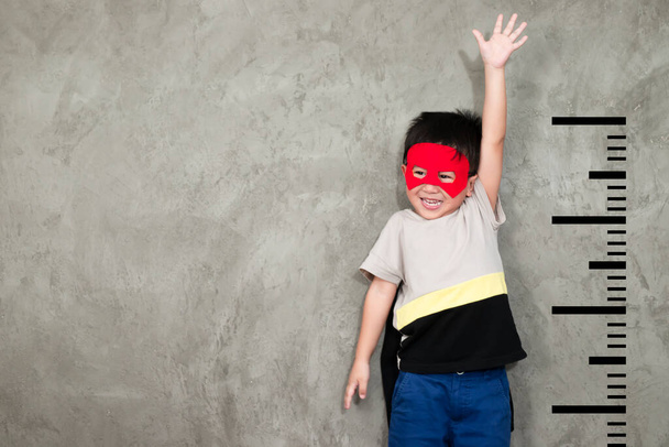 O menino da roupa de super-herói sorriu e levantou a mão para mostrar o crescimento, com uma unidade ao seu lado
 - Foto, Imagem