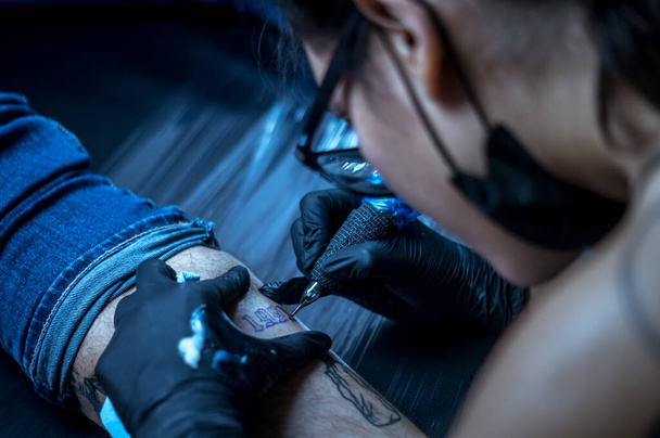 художница в очках, татуирующая ногу
 - Фото, изображение
