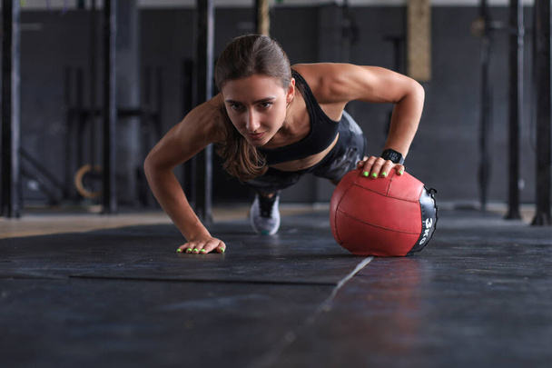 Подтянутая и мышечная женщина занимается с мячом в тренажерном зале - Фото, изображение