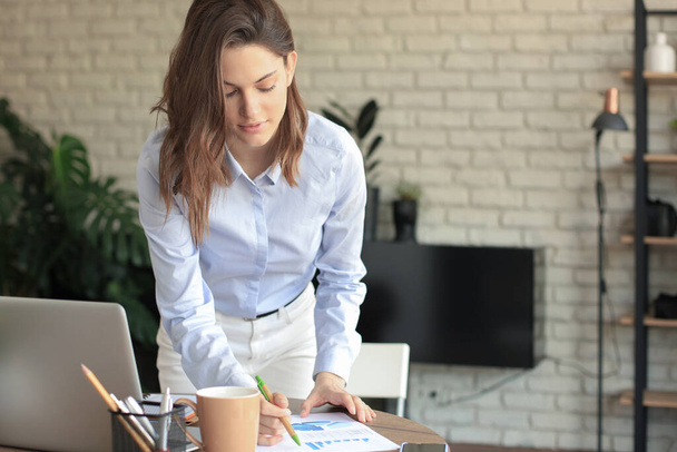 Young business woman standing in her home office reading notes - Foto, Imagen