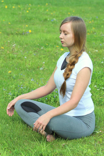 Young woman of European appearance does yoga in summer nature. Woman sitting in easy pose, sukhasana. High quality photo for web and print with empty space for text and design. - Foto, imagen