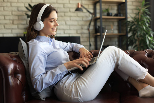 Smiling young woman with headphones and laptop on the sofa - Foto, immagini