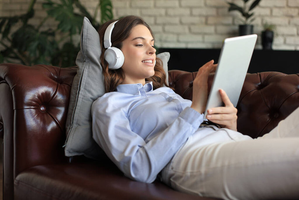 Smiling young woman with headphones and digital tablet on the sofa - Foto, imagen