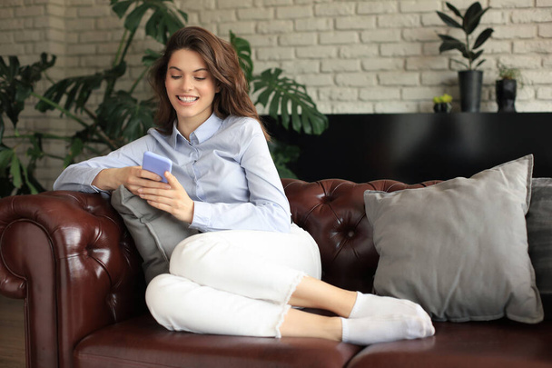 Pretty girl using her smartphone on couch at home in the living room - Photo, image