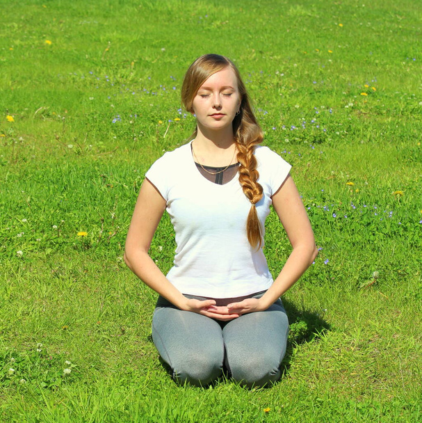 Young woman of European appearance does yoga in summer nature. Woman sitting on her knees in vajrasana, thunderbolt pose. High quality photo for web and print with empty space for text and design. - Photo, image