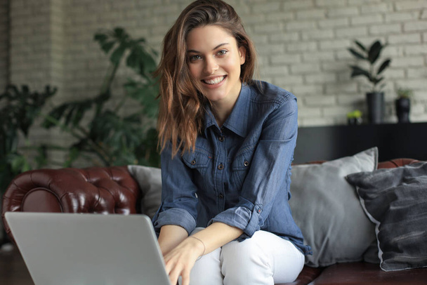 Smiling young woman sitting on sofa with laptop computer and chating with friends - Foto, Imagem
