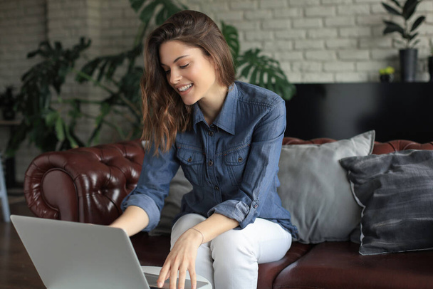 Smiling young woman sitting on sofa with laptop computer and chating with friends - Фото, зображення