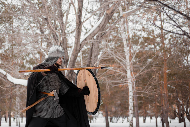 Viking in inverno con una lancia e uno scudo rotondo di colore rosso-nero. Un ragazzo con il casco e la catena nella neve
. - Foto, immagini