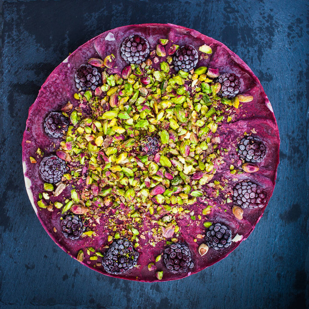 黒果実とピスタチオの入った健康的な砂糖なし生ケーキ暗い花崗岩の背景に平らなレイアウト健康的な食品の概念 - 写真・画像