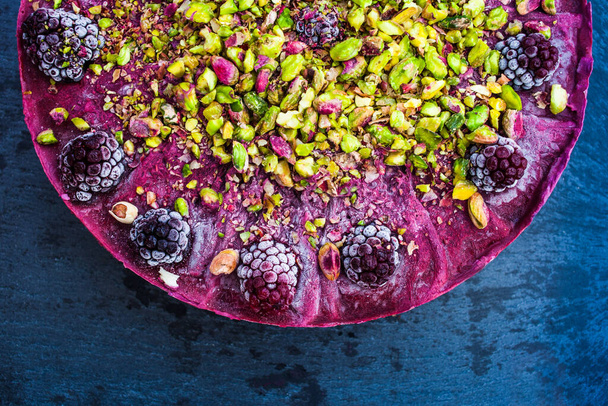 close up of healthy raw cake with  blackberries and pistachios flat lay on dark granite background healthy food concept - Photo, Image