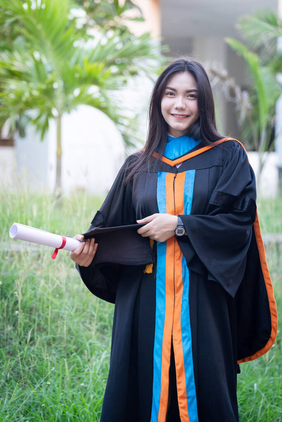 Portrait of happy and excited young Asian female university graduate wears graduation gown and hat celebrates with a degree in the university campus on the commencement day. Education concept. - Foto, Imagem