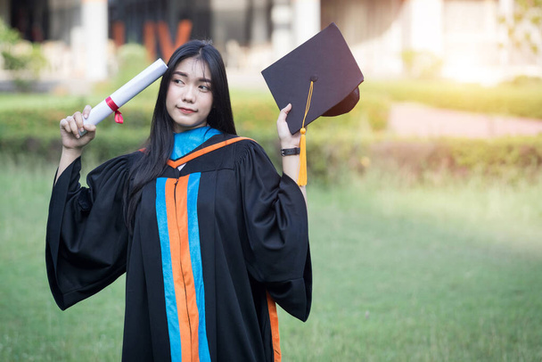 幸せな興奮した若いアジアの女性大学卒業生の肖像画は卒業のガウンを身に着けており、帽子は開始日に大学のキャンパスで学位を祝う。教育理念. - 写真・画像