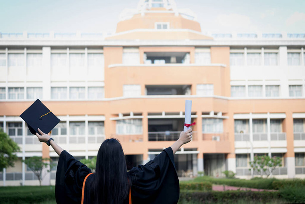 Πορτρέτο του χαρούμενος και ενθουσιασμένος νεαρή ασιατική απόφοιτος πανεπιστημίου φοράει φόρεμα αποφοίτησης και καπέλο γιορτάζει με πτυχίο στην πανεπιστημιούπολη την ημέρα έναρξης. Εκπαιδευτική έννοια. - Φωτογραφία, εικόνα