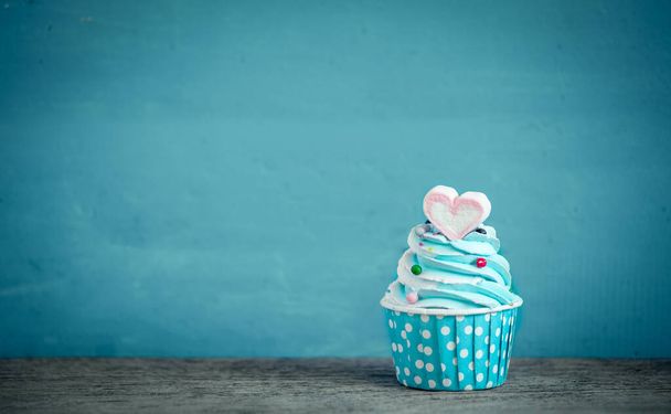 Cupcake con dulce forma de corazón de malvavisco sobre fondo azul
 - Foto, Imagen