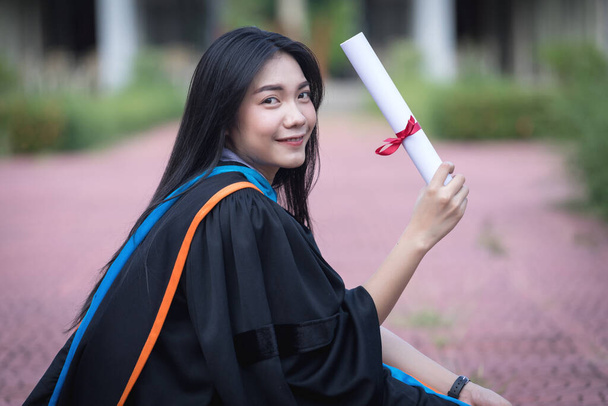Portrait of happy and excited young Asian female university graduate wears graduation gown and hat celebrates with a degree in the university campus on the commencement day. Education concept. - Foto, Imagem