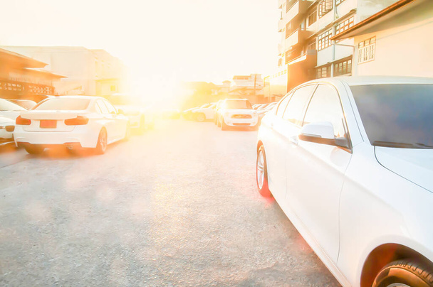 都会の駐車場に停められた現代的なきれいな輝きの白い車の多くは、背景に輝く夕日。背景色が悪い. - 写真・画像