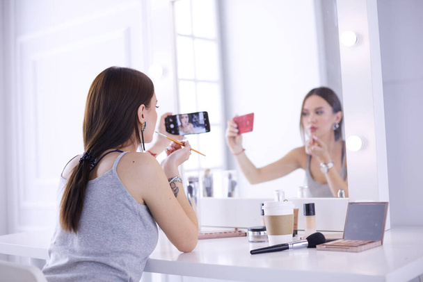 Beauty blogger filming makeup tutorial with smartphone in front of mirror - Valokuva, kuva