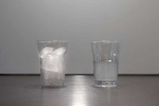 IJsblokjes smelten in glas of plastic bekertje waaruit blijkt dat de fysische toestand van water verandert van ijs naar vloeistof. Eén kopje met ijs. Een kopje met water - Foto, afbeelding