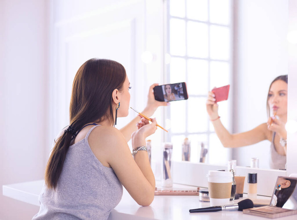 Beauty blogger filming makeup tutorial with smartphone in front of mirror - Foto, imagen