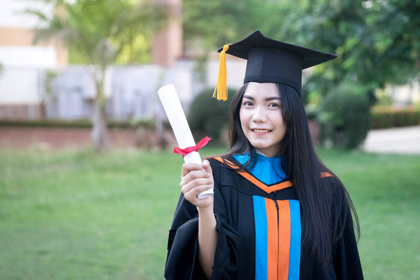 Retrato de la joven universitaria asiática feliz y emocionada graduada lleva vestido de graduación y sombrero celebra con un título en el campus de la universidad en el día de inicio. Concepto educativo
. - Foto, Imagen