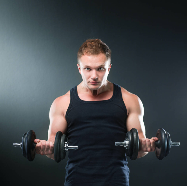 Closeup of a muscular young man lifting weights on dark background - Photo, image
