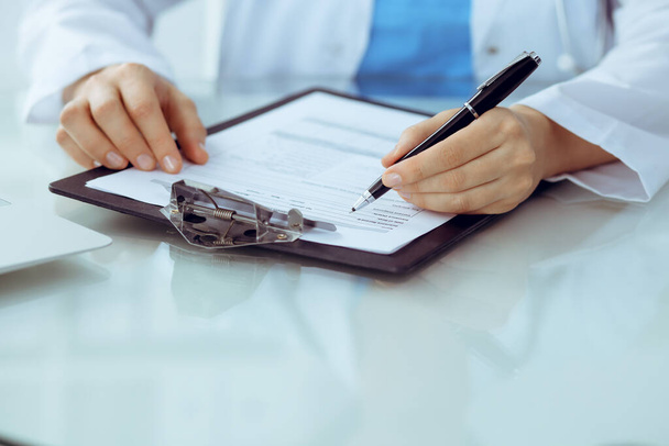 Doctor woman filling up medical form while sitting at the table, close-up of hands - Foto, imagen