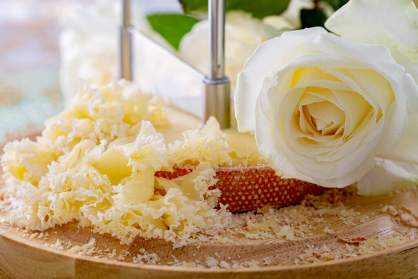 Szwajcarski ser z okruszkami na drewnianej, okrągłej powierzchni i piękną białą różą. Zamazane tło i bokeh. Miękkie skupienie. - Zdjęcie, obraz
