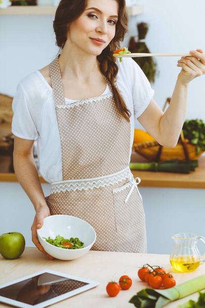 Young brunette woman cooking in kitchen. Housewife holding wooden spoon in her hand. Food and health concept - Fotó, kép