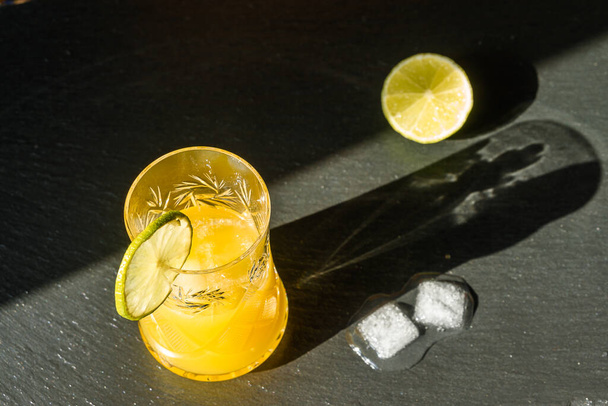 Cold summer delicious coctail with lime and ice in a glass with drops on the black stone background. - Foto, afbeelding