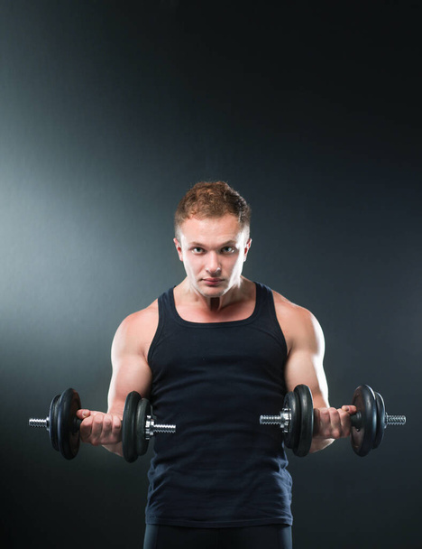 Closeup of a muscular young man lifting weights on dark background - Valokuva, kuva