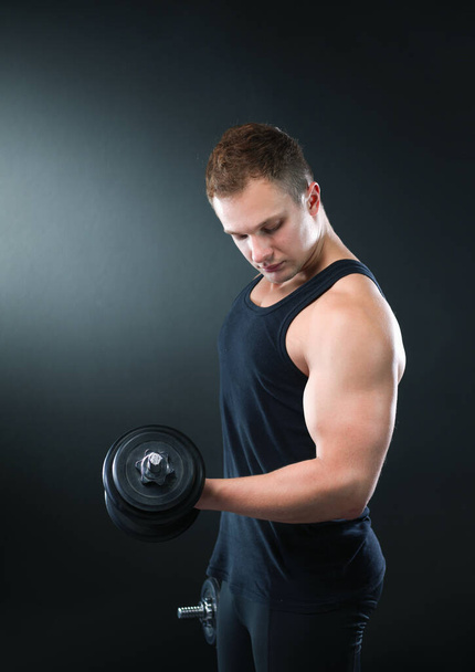 Closeup of a muscular young man lifting weights on dark background - Фото, зображення