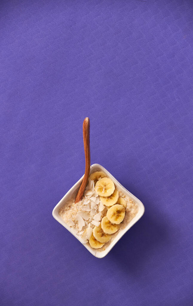 Bowl of porridge sitting on yoga mat topped with banana and coconut. - Photo, Image