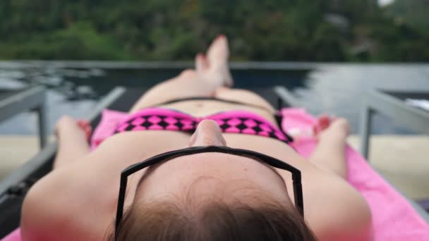 mladá žena v bikinách a slunečních brýlích relaxuje na lehátku - Záběry, video