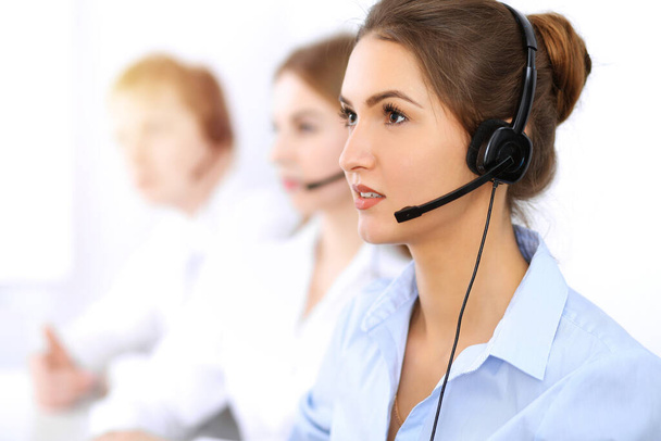 Call center. Focus on beautiful business woman using headset in sunny office - Foto, Bild
