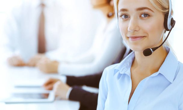 Group of diverse phone operators at work in sunny office. Handsome business woman with headphones consulting clients. Call center and business people concept - Фото, зображення