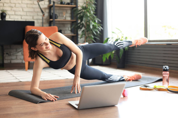 Fitness beautiful slim woman doing side plank and watching online tutorials on laptop, training in living room. Stay at home activities. - Fotó, kép