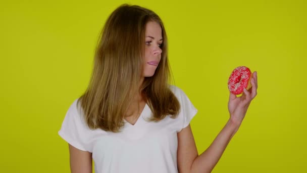Vrouw in een wit T-shirt kijkt naar de rode donuts in de hand, likt en bijt lippen - Video
