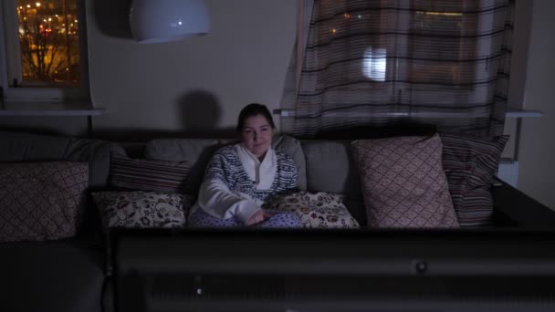 Young woman sits on a couch in front of the TV in the dark - Footage, Video