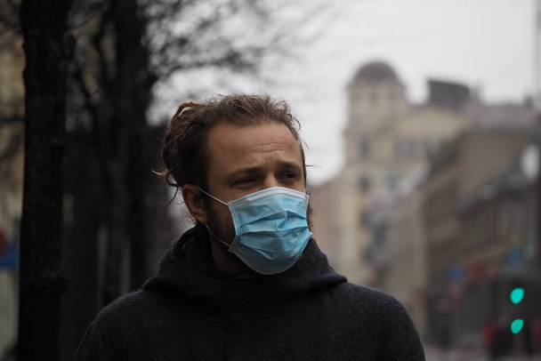 Красивый молодой европейский мужчина в зимней одежде на улице в медицинской маске. Крупный план 35-летнего мужчины в респираторе для защиты от инфекции вирусом гриппа или коронавирусом - Фото, изображение