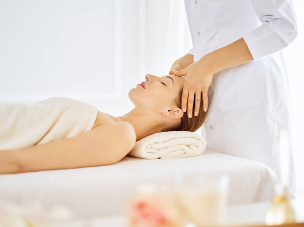 Beautiful woman enjoying facial massage with closed eyes in spa center. Relaxing treatment concept in medicine - Foto, Imagem