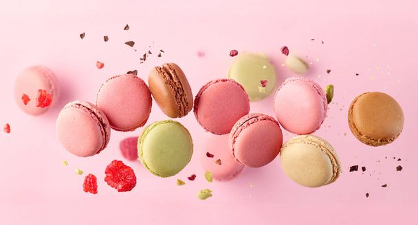 various colorful macaroons in motion falling on pink background. Sweet and colourful french macaroons falling or flying in motion - Photo, Image