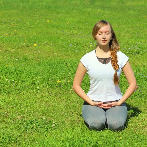 Young woman of European appearance does yoga in summer nature. Woman sitting on her knees in vajrasana, thunderbolt pose. High quality photo for web and print with empty space for text and design. - Fotó, kép