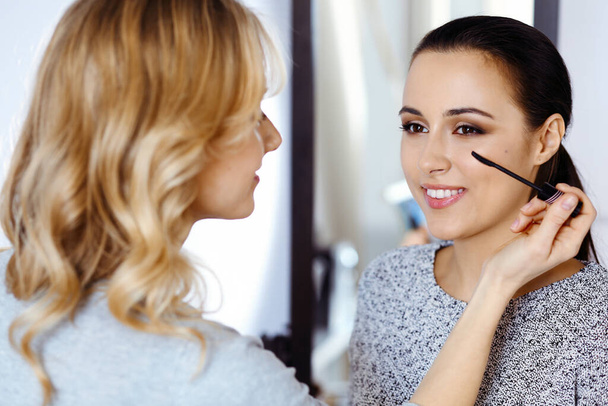 Professional makeup artist working with beautiful young woman. Bridal, fashion or nude style - Photo, Image