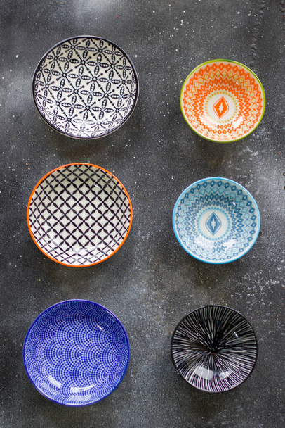 Colorful bowls on the black background, kitchen equipment on the table, bowl with geometric design. - Photo, Image