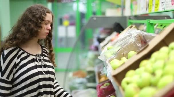Buying pears in a supermarket. A young girl chooses ripe fruit on a shelf in a store. - Video