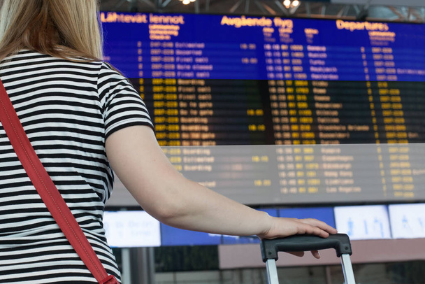 Woman looks at the scoreboard at the airport. Select a country Estonia for travel or migration. - Photo, Image