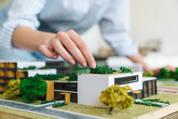 Cropped photo of young woman architect designing draft with house model at workplace - 写真・画像