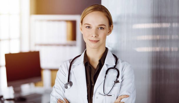 Cheerful smiling female doctor standing with arms crossed in clinic. Portrait of friendly physician woman. Medicine concept - Фото, зображення